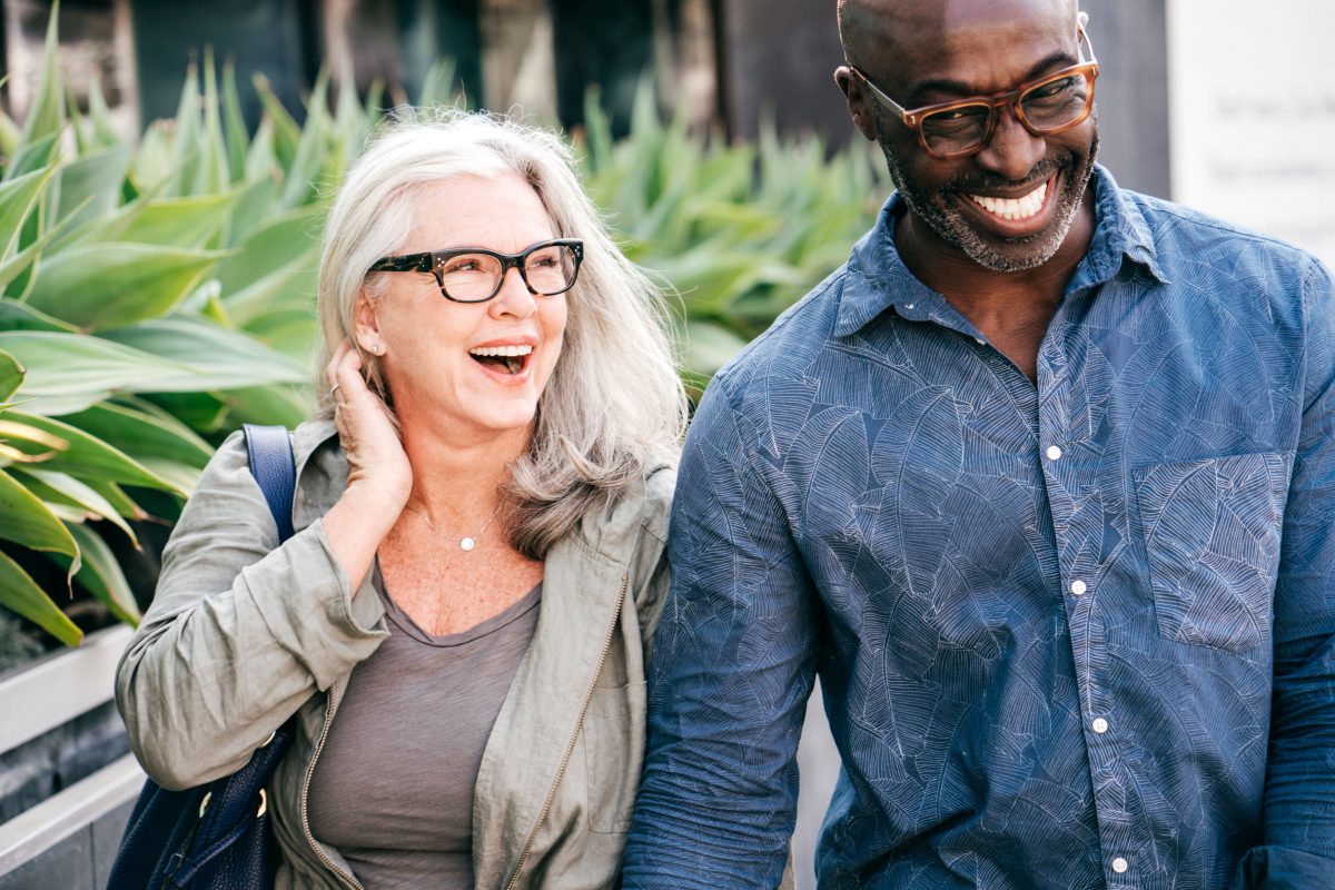 elder interracial couple holding hands and shopping bags laughing outdoors while shopping