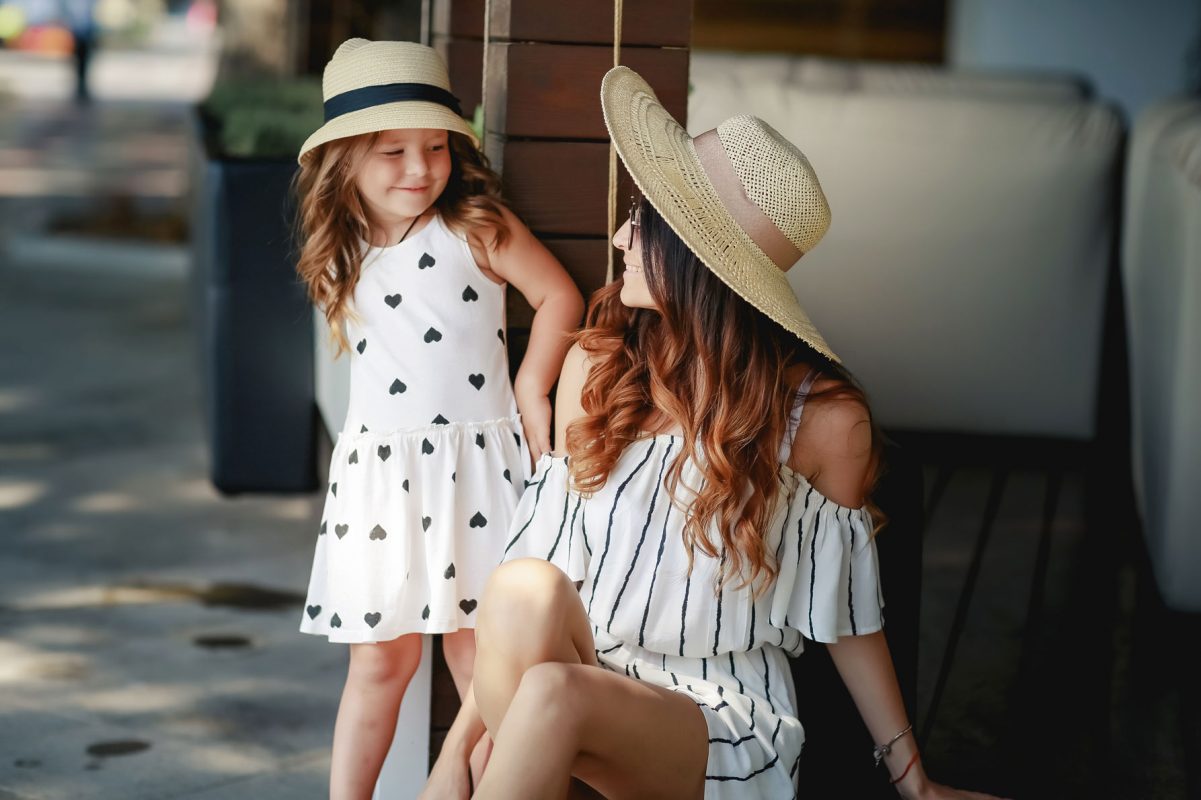young mother and daughter in sundresses and sunhat outdoors in the city