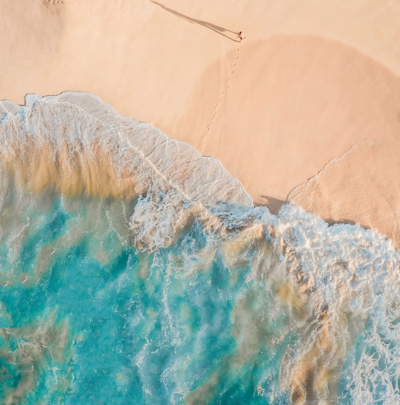 turquoise waves breaking on the beach with person walking leaving footprints